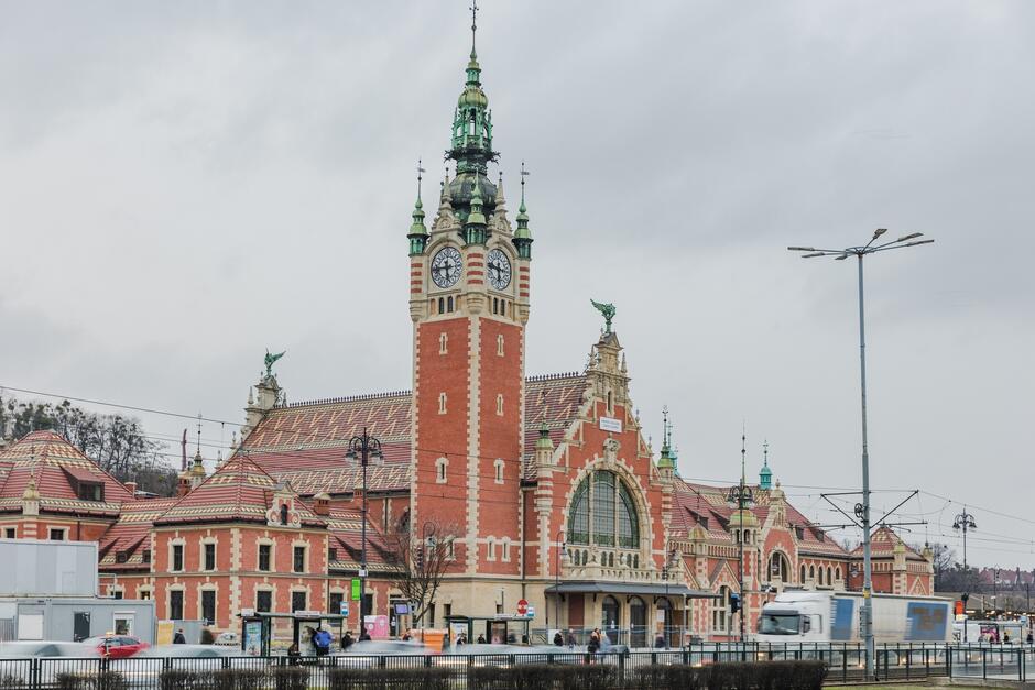na zdjęciu odnowiony zabytkowy budynek dworca kolejowego w gdańsku, widać ceglaną elewację i obok budynku wysoką wieżę zegarową
