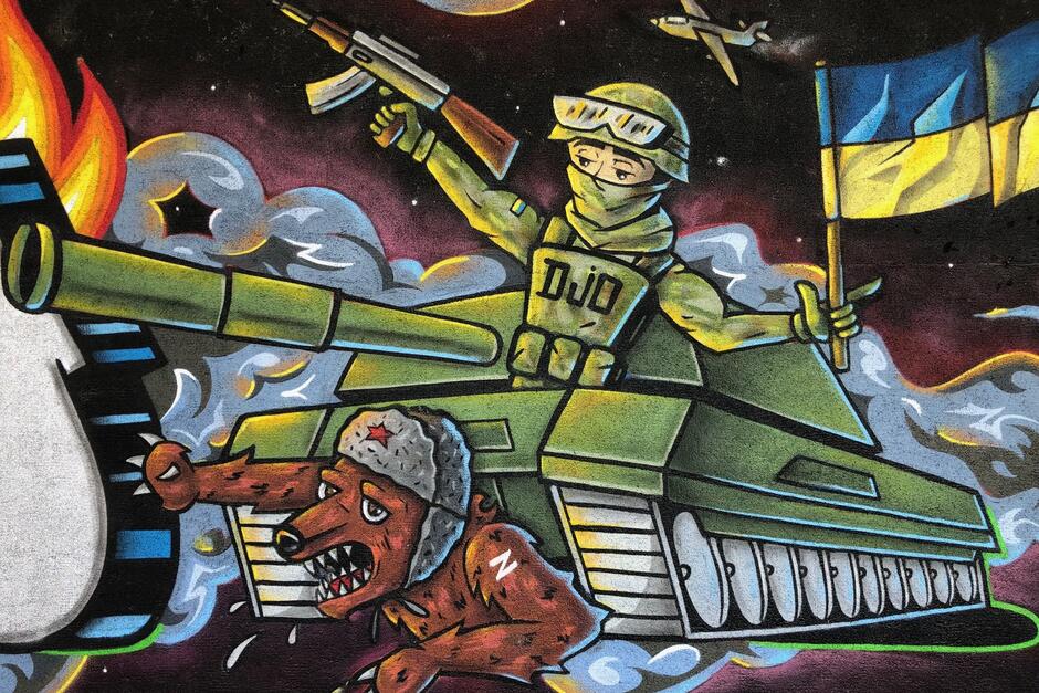 Mural przedstawia ukraińskiego żołnierza z karabinem, który siedzi w wieżyczce czołgu z zatkniętą niebiesko-żółtą flagą. Czołg rozjeżdża wilka, który rozpaczliwie próbuje uciec spod gąsiennic pojazdu. Wilk ma na czapce czerwoną gwiazdkę 