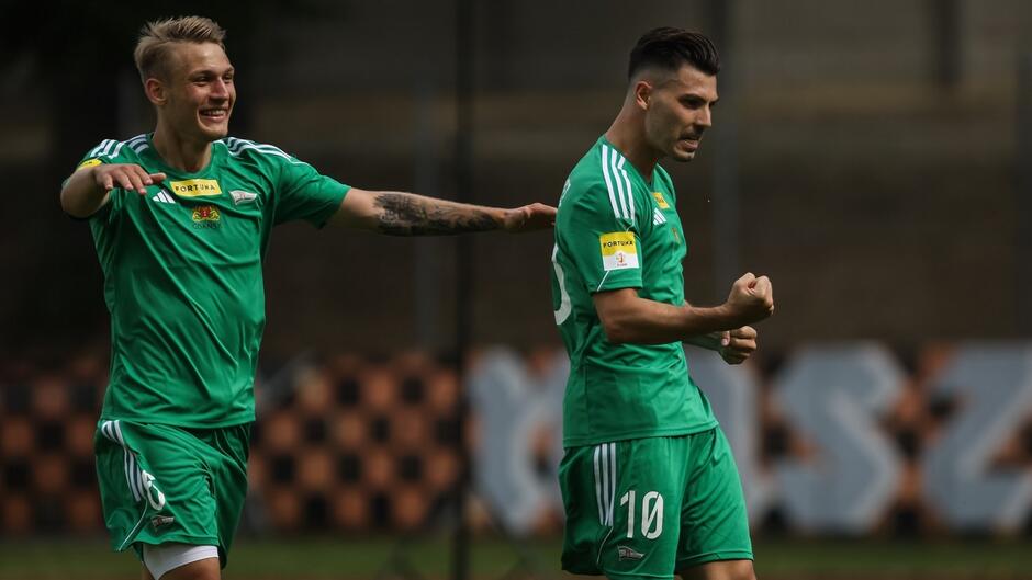 Dwóch piłkarzy obok siebie, cieszą się