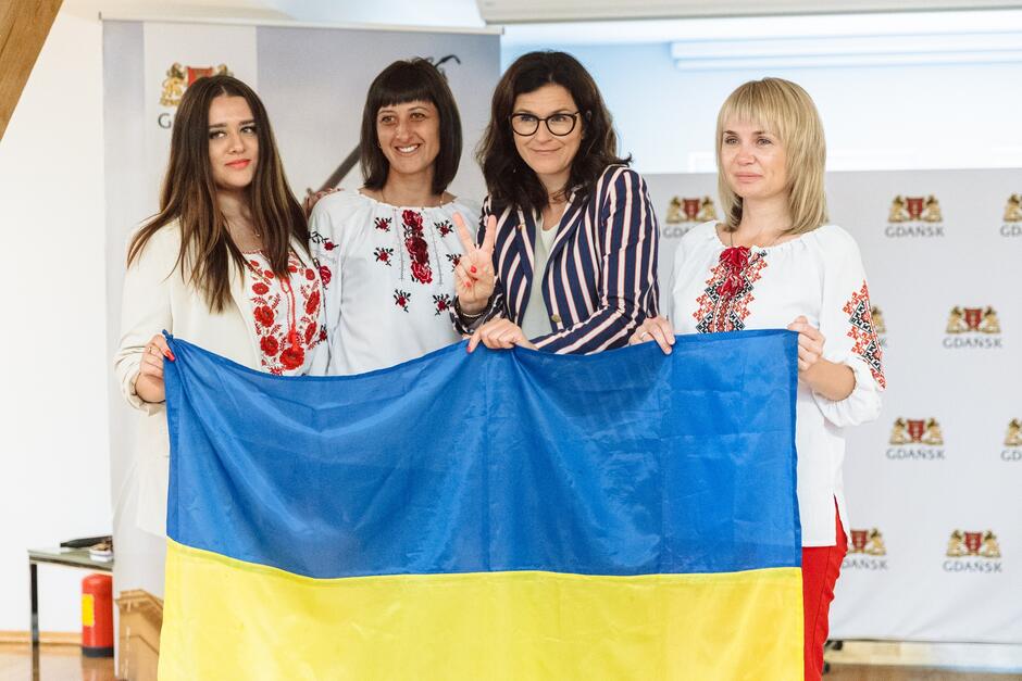 wymienione kobiety trzymają dużą flagę Ukrainy