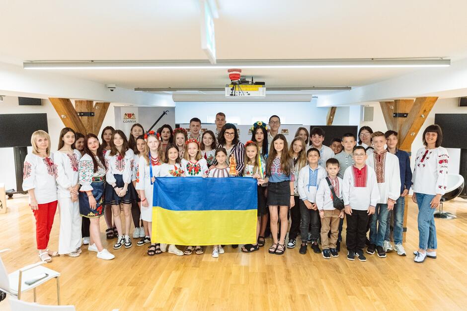 kilkadziesiąt osób, dzieci,młodzież i dorośli pozują z flagą Ukrainy