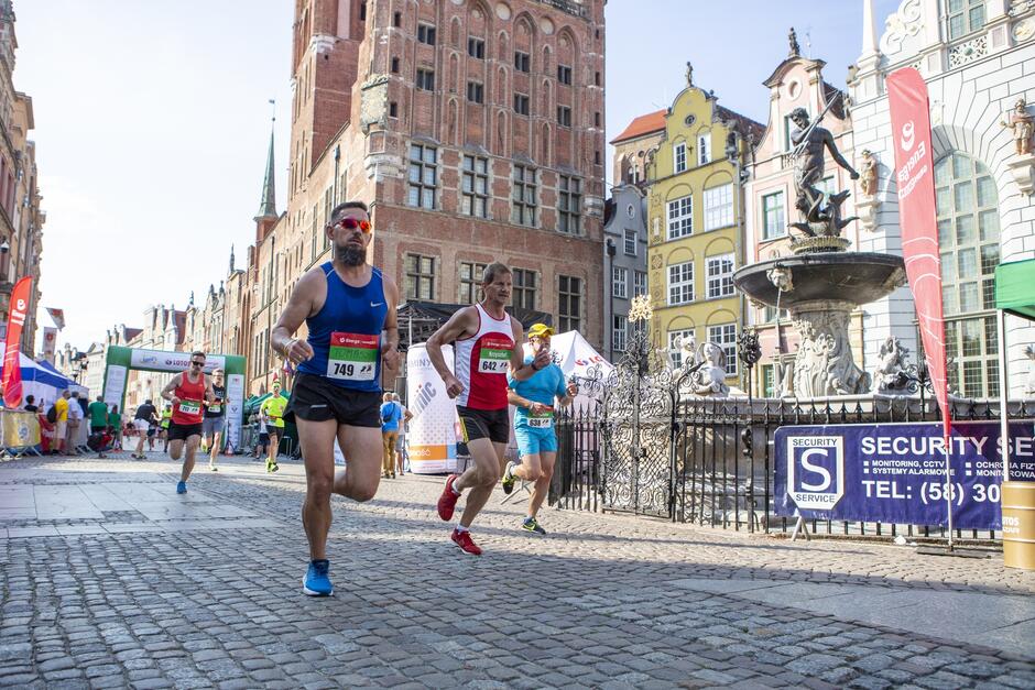 Kilku biegaczy na ulicy, obok Fontanna Neptuna i stare miejskie kamienice