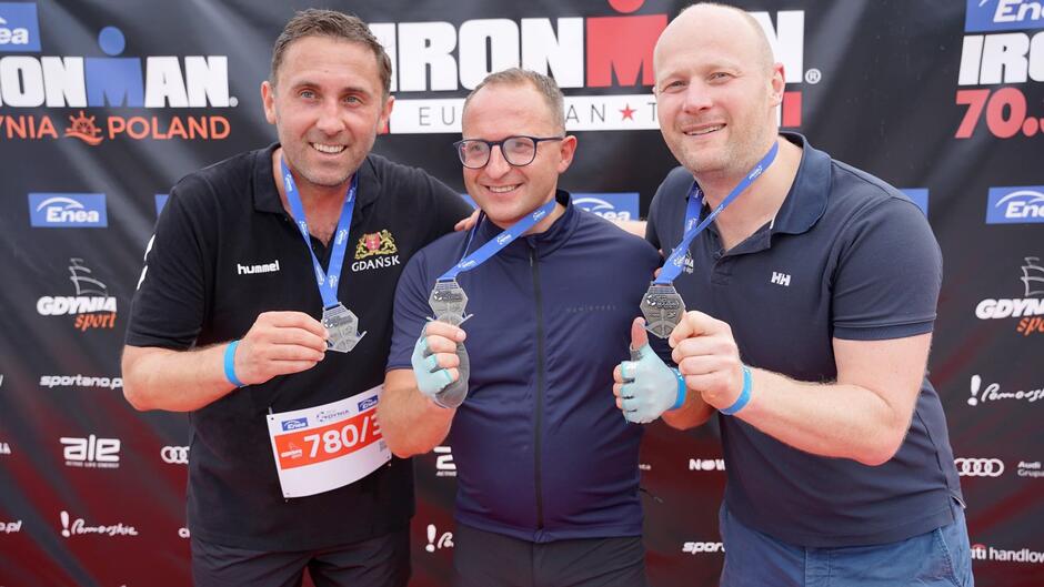 Trzech mężczyzn w strojach sportowych prezentujących zdobyte medal