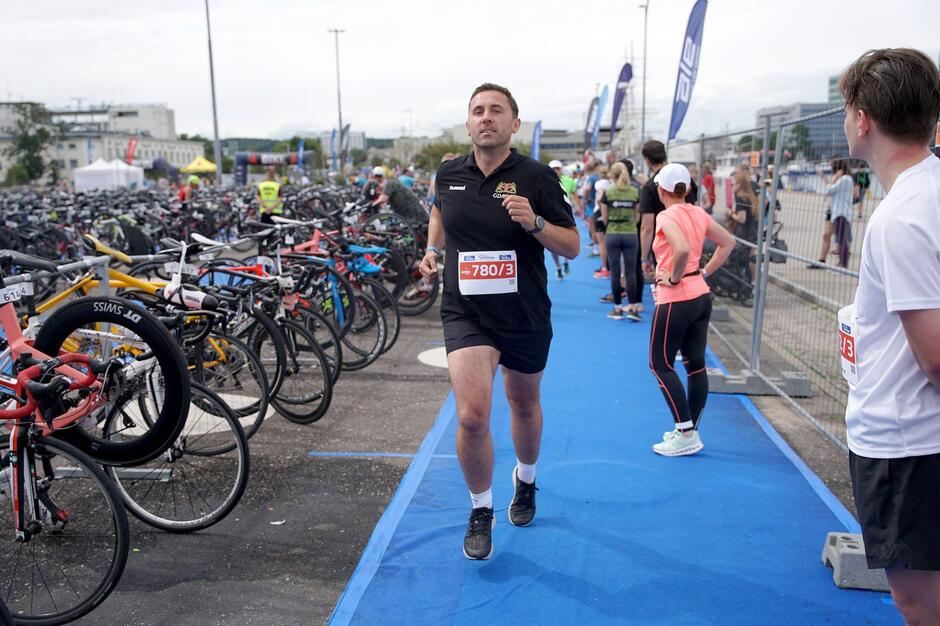 Mężczyzna biegnący na bieżni na plaży, obok zaparkowanych kilkudziesięciu rowerów