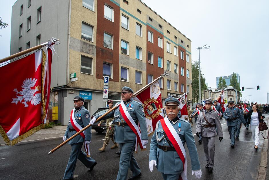 Mężczyźni w mundurach idą z biało-czerwonymi sztandarami