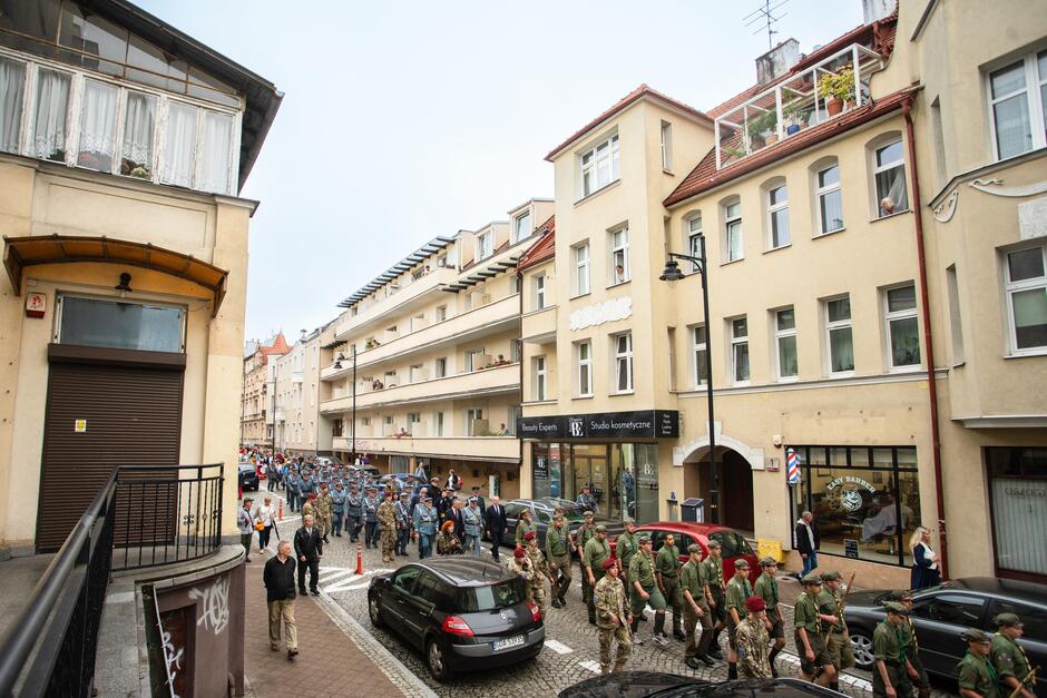 Kolumna osób ze sztandarami idzie środkiem ulicy we Wrzeszczu. W tle widać Galerię Bałtycką