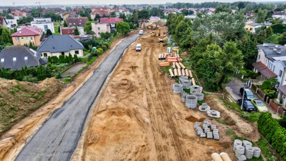 zdjęcie z drona, widać nowo położoną drogę asfaltową, po prawej teren gruntowy, w tle zabudowania jednorodzinne