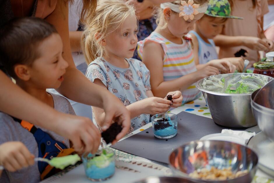 Mała dziewczynka i inne dzieci siedzą przy stole i układają kolorowe jedzenie w salaterkach i miseczkach