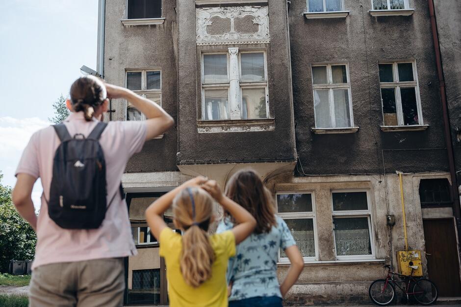 Mężczyzna i dzieci stoją na chodniku z zadartą głową, patrzą na budynek