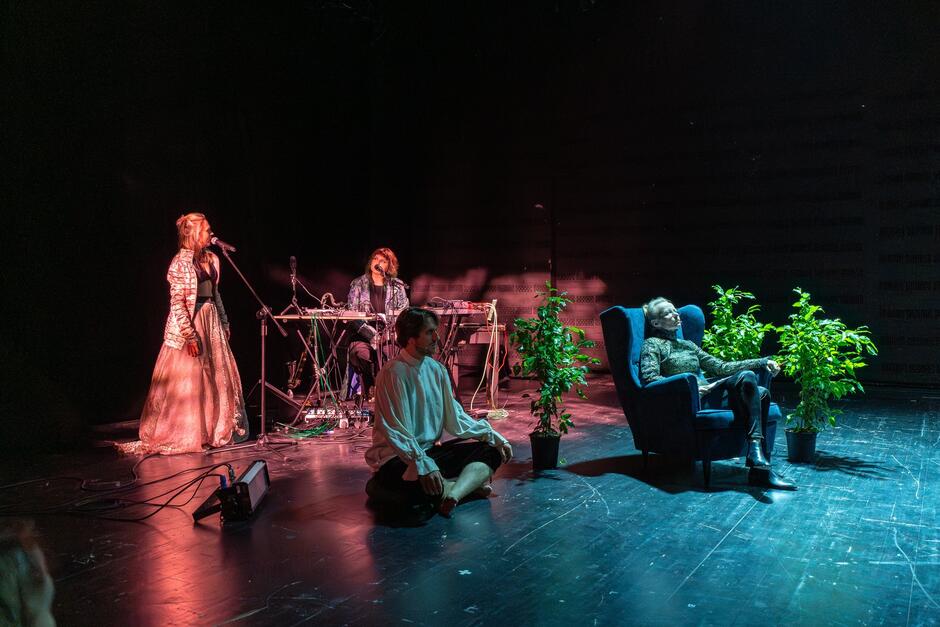 scena teatralna, na niej cztery osoby, jedna śpiewa do mikrofonu, druga tworzy muzykę na żywo, dwie osoby siedzą