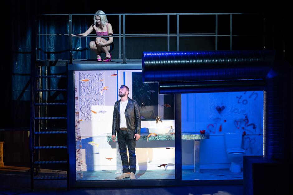 platforma na scenie, na balkonie kuca młoda dziewczyna, pod nim stoi młody mężczyzna w skórzanej kurtce