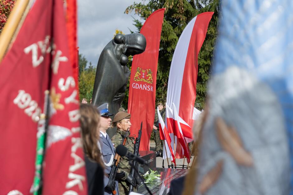 Zdjęcie przedstawia dwóch żołnierzy na warcie przy pomniku Golgota Wschodu na Cmentarzu Łostowickim, wokół nich są liczne biało-czerwone flagi 