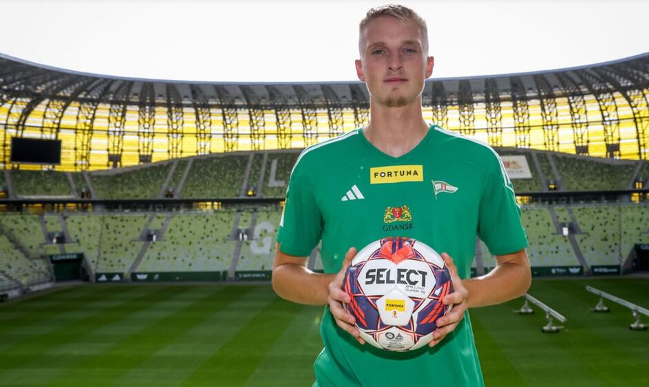Młody mężczyzna na tle stadionu piłkarskiego. trzyma w rękach zielono-białą koszulkę z numerem 3