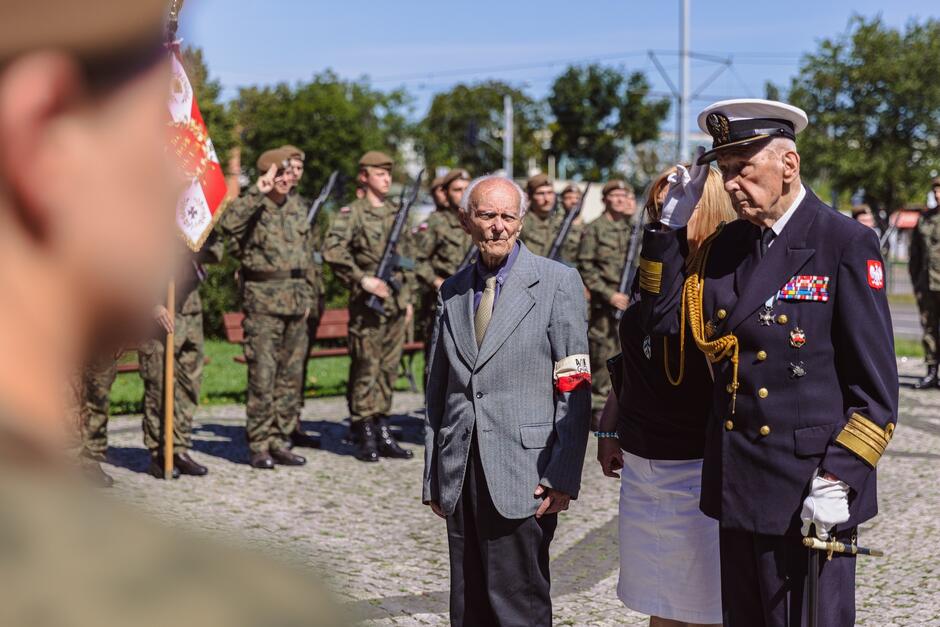 na zdjęciu dwóch starszych mężczyzn w żołnierskich strojach salutuje przed pomnikiem, którego akurat nie widać na zdjęciu