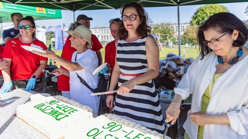 Kilka osób krojących tort z nazwą 90-lecie Olszynki