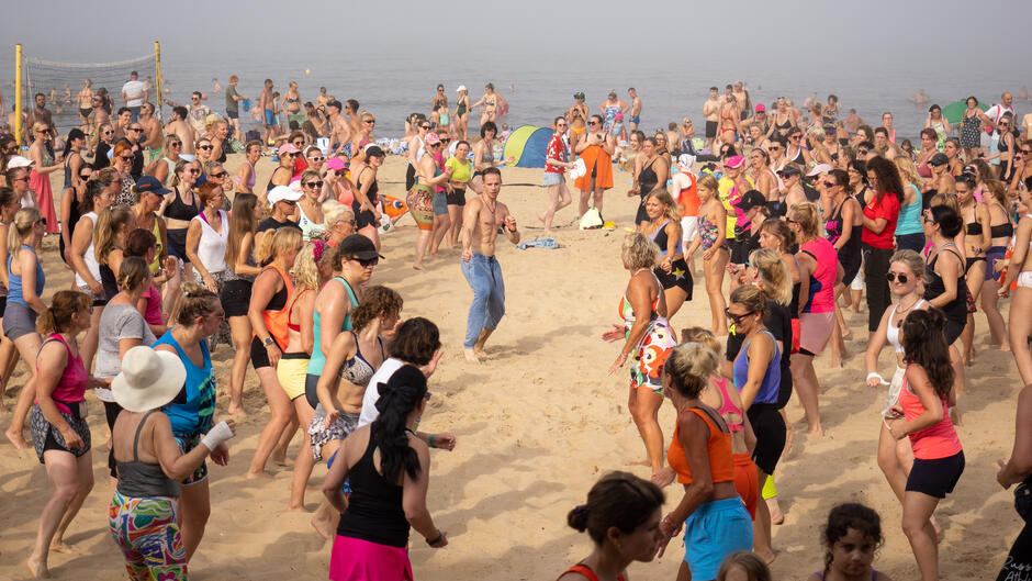 Kilkaset osób tańczy na plaży, w środku mężczyzna z gołym torsem w spodniach