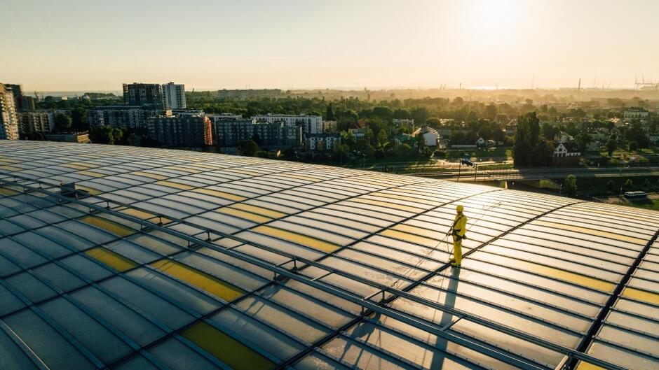 mężczyzna w stroju roboczym trzyma w ręku urządzenie do mycia i stoi na dachu stadionu