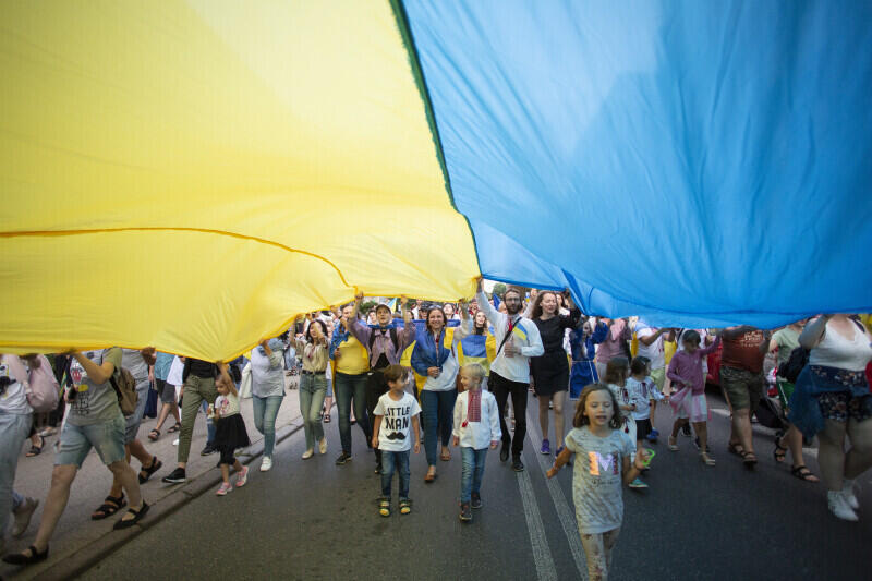 grupa osób niesie ogromną niebiesko-żółtą flagę