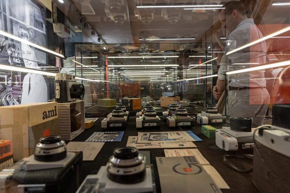 gablota szklana z aparatami fotograficznymi nad którą stoi mężczyzna