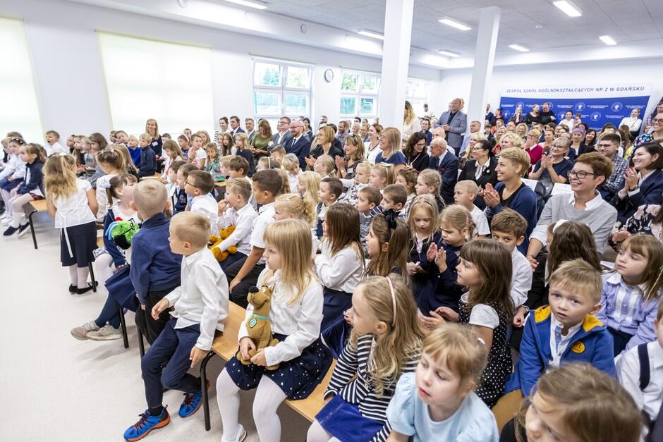 dzieci galowo ubrane siedzą w dużej sali