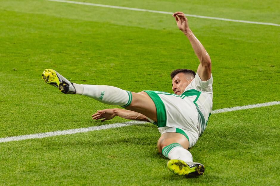 Piłkarz w jasnym stroju na ziemi z nogą wysuniętą do przodu
