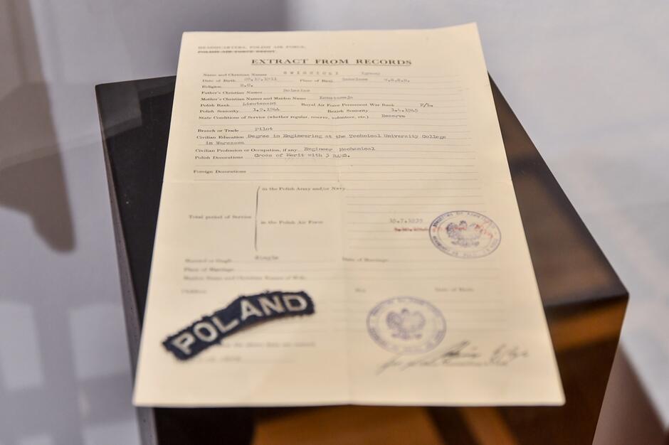 Dokument służby w PAF w języku angielskim, obok naszywka z napisem Poland
