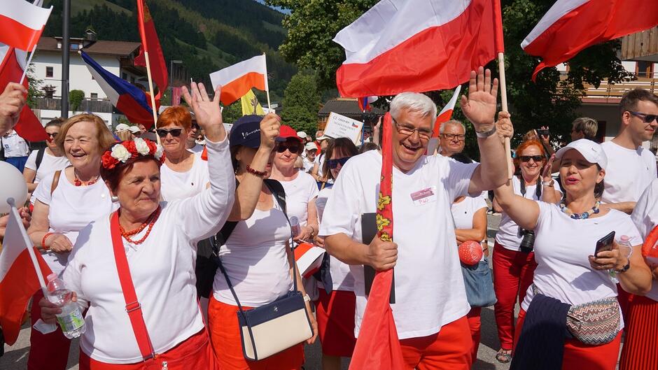 grupa ludzi ubranych w czerwone spodnie lub spódnice i białe koszulki, z flagami Polski i gdańska 