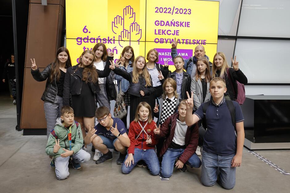 Kilkanaście osób, młodzież - stoją przed planszą z napisem Gdański Tydzień Demokracji i Lekcje Obywatelskie 