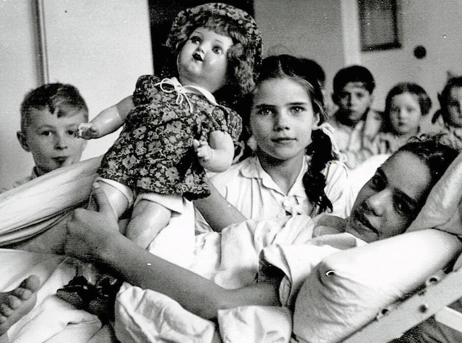 Czarno-białe zdjęcie, kilkoro dzieci w szpitalu z lalką