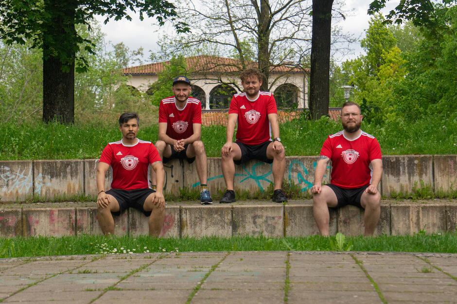czterech mężczyzn w czerwonych koszulkach sportowych, siedzą na zewnątrz