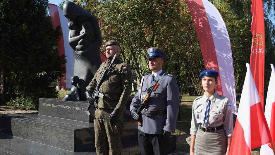 Żołnierz, policjant i harcerka stojący na baczność przed pomnikiek