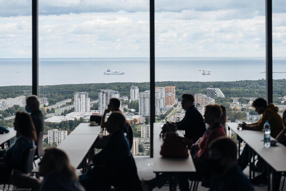 Widok z wysokiego piętra na morze ze statkami i salę z ludźmi przy stołach