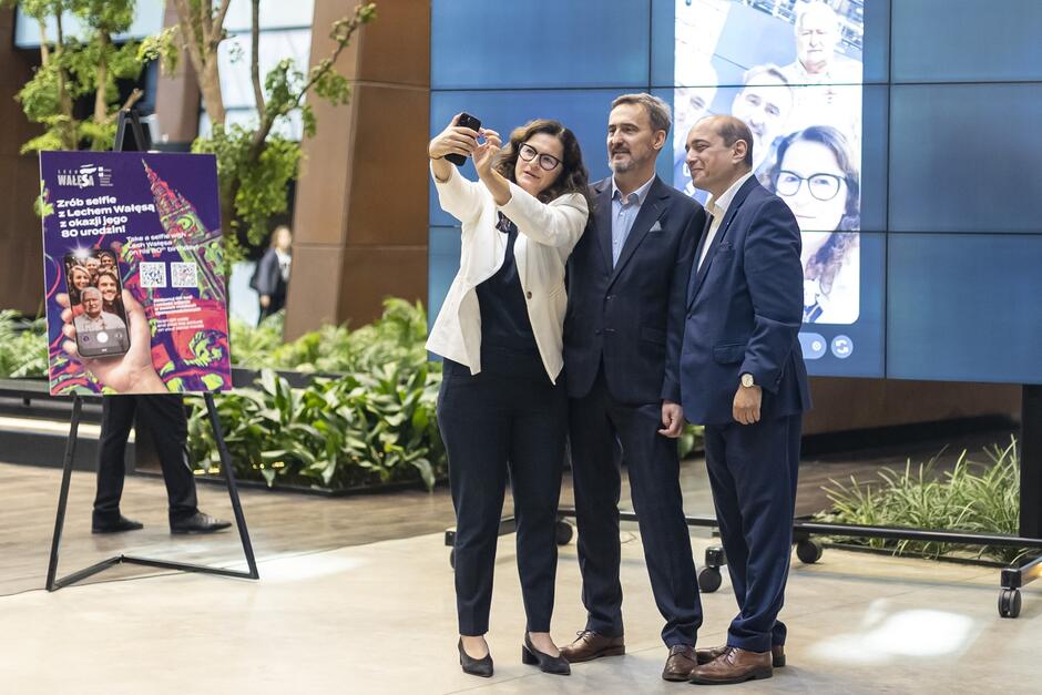dwóch mężczyzn i kobieta robią sobie selfie telefonem