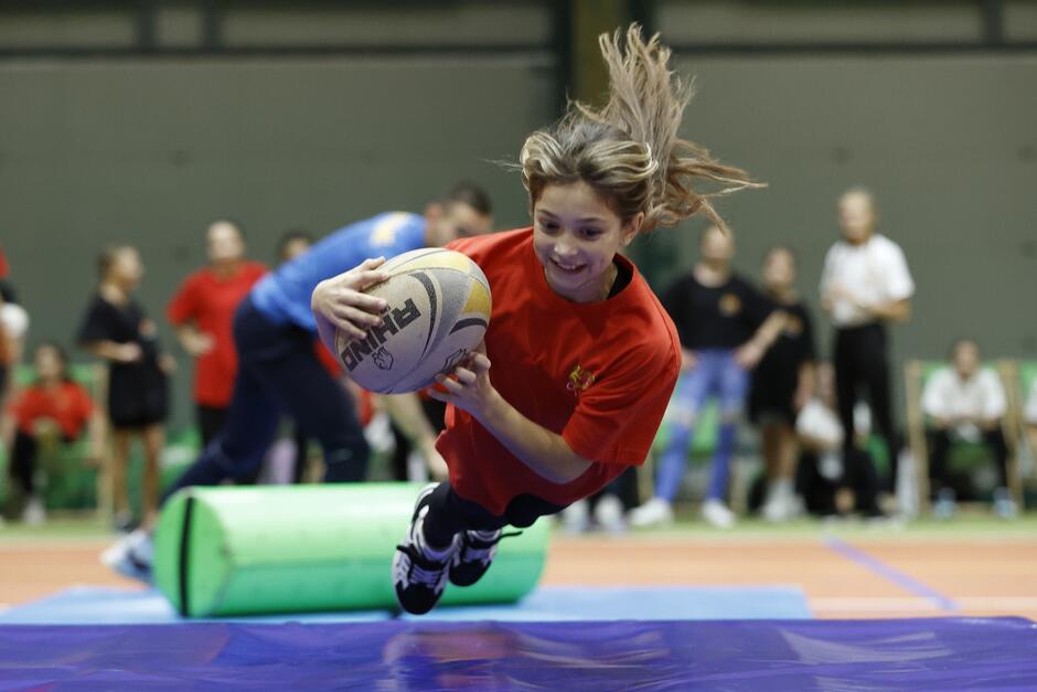młoda dziewczyna uchwycona w ruchu, gdy rzuca się na materac z piłką do rugby