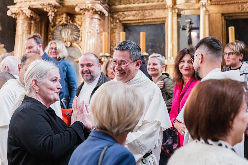 zakonnik w białej szacie uśmiecha się i rozmawia z kobietami w kościele