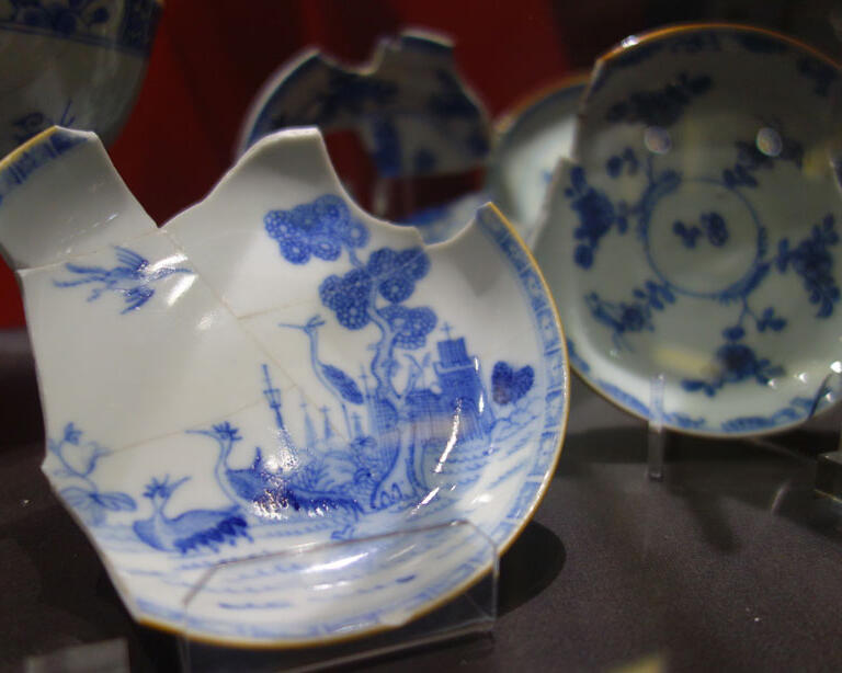 Potłuczone talerze porcelanowe z niebieskimi rysunkami prezentowane na stołach