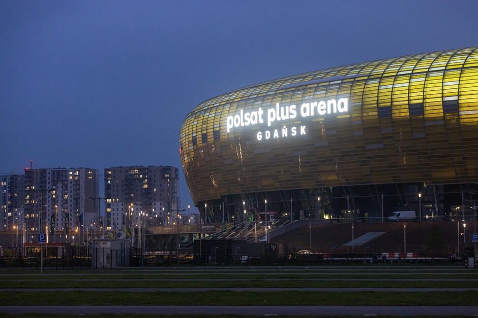 Okrągły budynek stadionu sfotografowany nocą, na koronie widnieje napis Stadion Polsat Plus Arena Gdańsk