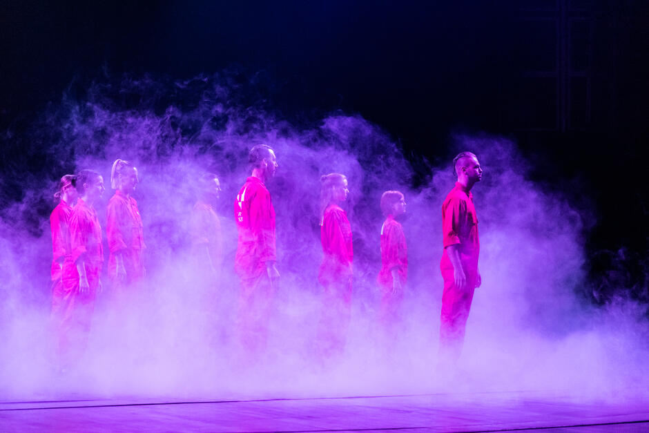 tancerze w czerwonych kombinezonach na scenie spowitej dymem