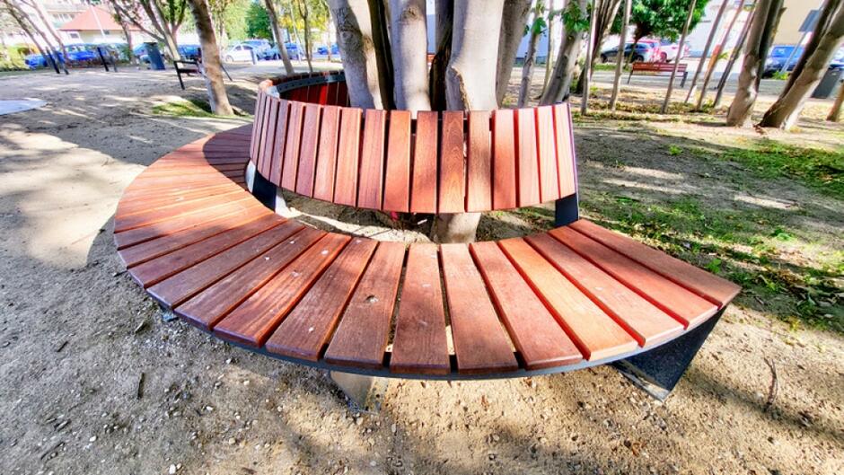 na zdjęciu półokrągła drewniana ławka zbudowana wokół rosnącego drzewa