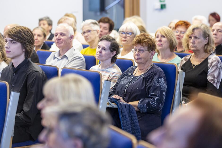 na zdjęciu kilkadziesiąt starszych osób, siedzą na krzesłach, w kilkunastu rzędach, patrzą przed siebie