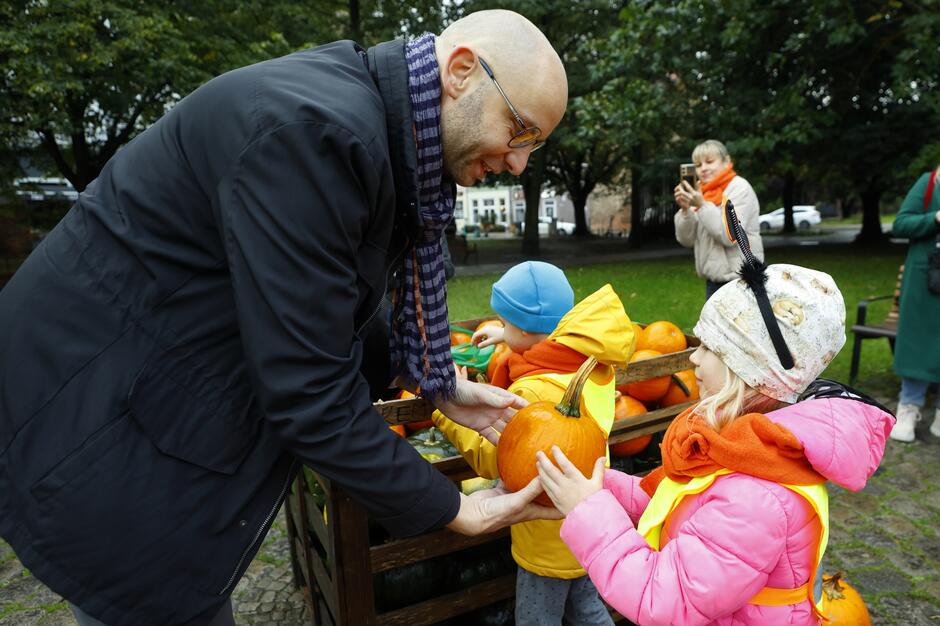 Piotr Kryszewski rozdaje dynie dzieciom biorącym udział w akcji dekorowania Placu Kobzdeja. 