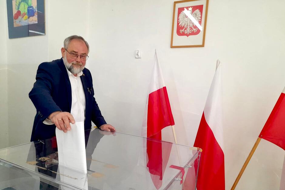 Mężczyzna po sześćdziesiątce, brodaty i w okularach, wrzuca kartę do urny wyborczej