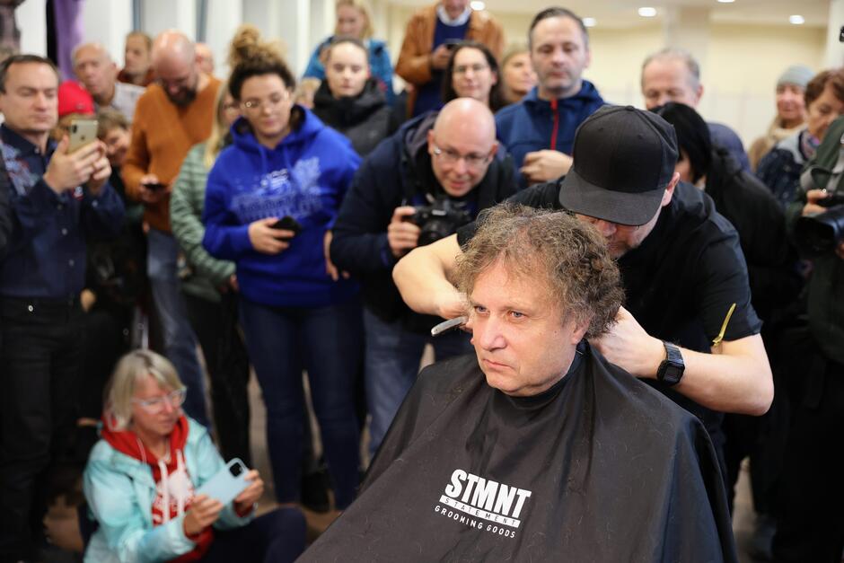 fryzjer strzyże długowłosego mężczyznę w średnim wieku