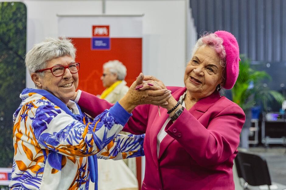 dwie starsze kobiety ubrane kolorowa tańczą w parze i uśmiechają się do zdjęcia