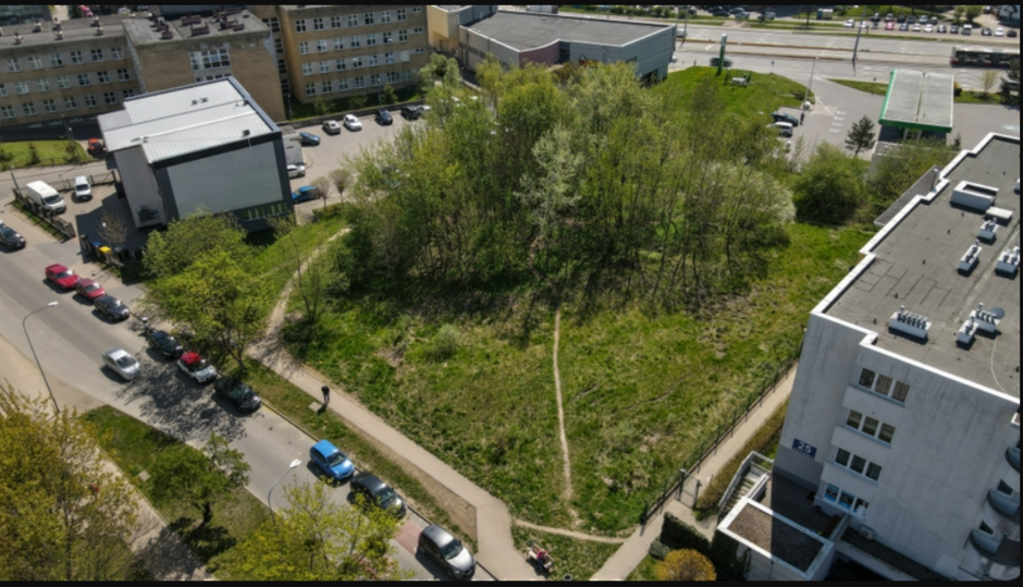 na zdjęciu zielony skwer z drzewami, wokół niego widać fragmenty budynków i ulicy, zdjęcie wykonane dronem