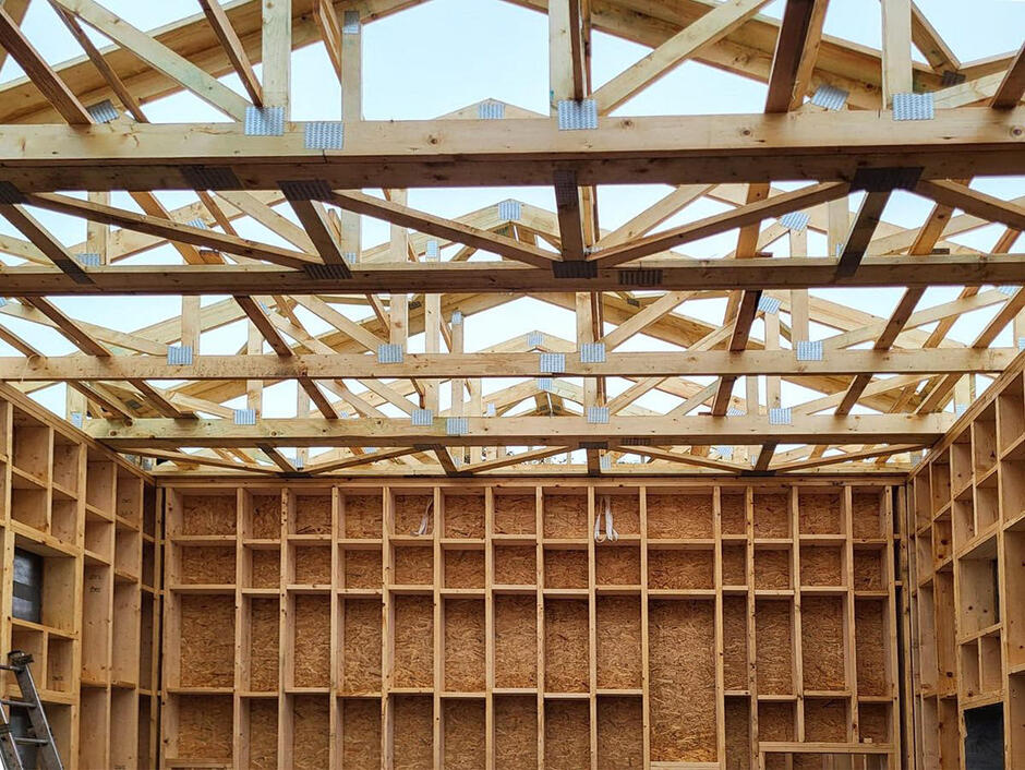 Na zdjęciu widać drewniany szkielet dachu budynku w budowie. Szkielet dachu składa się z belek i krat, które są połączone ze sobą, aby stworzyć solidną podstawę dla dachu