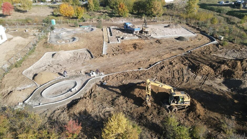 zdjęcie z drona, widać plac budowy, żółtą koparkę i rozkopany teren gruntowy