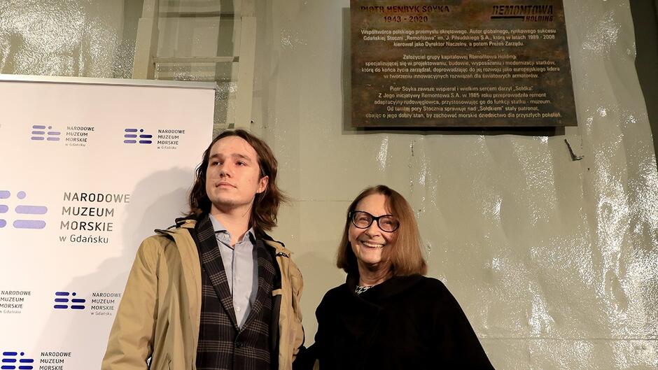 Młody mężczyzna i starsza kobieta pod tablicą upamiętniającą Piotra Soykę