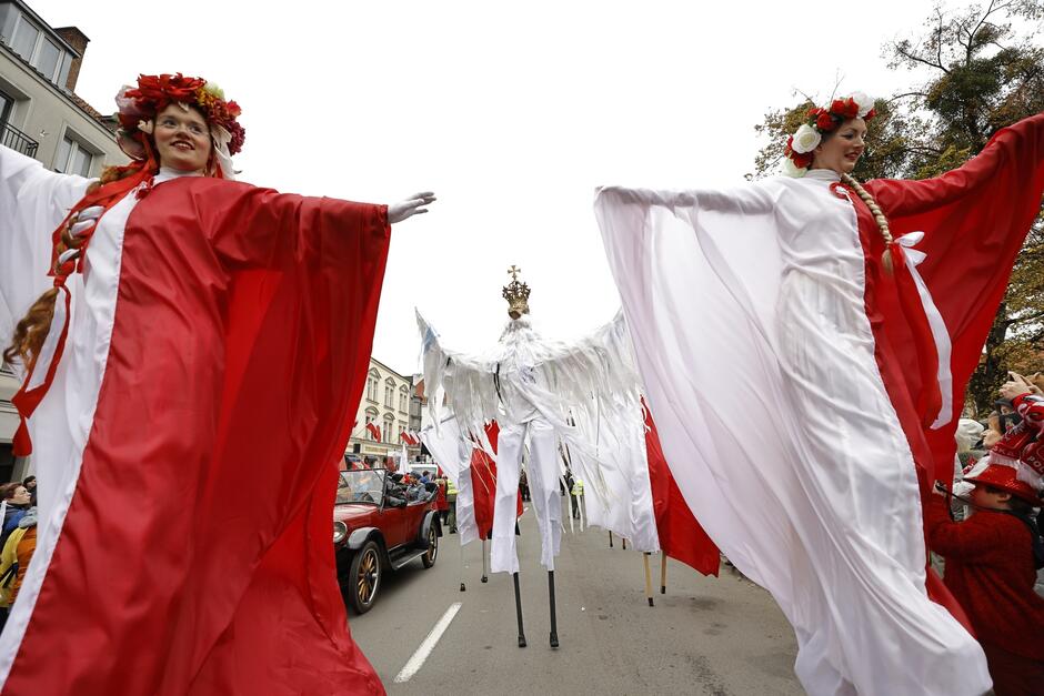 na zdjęciu dwie kobiety na szczudłach przebrane w biało czerwone stroje, a za nimi przebieraniec za białego orła