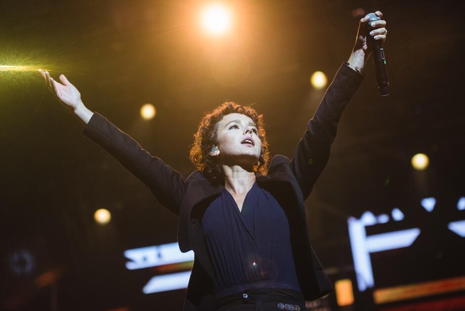 wokalistka na scenie z ramionami uniesionymi wysoko